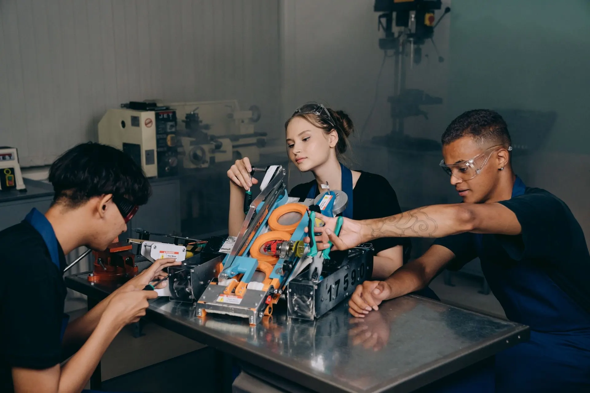 Three students fine-tune their competition robot in a workshop