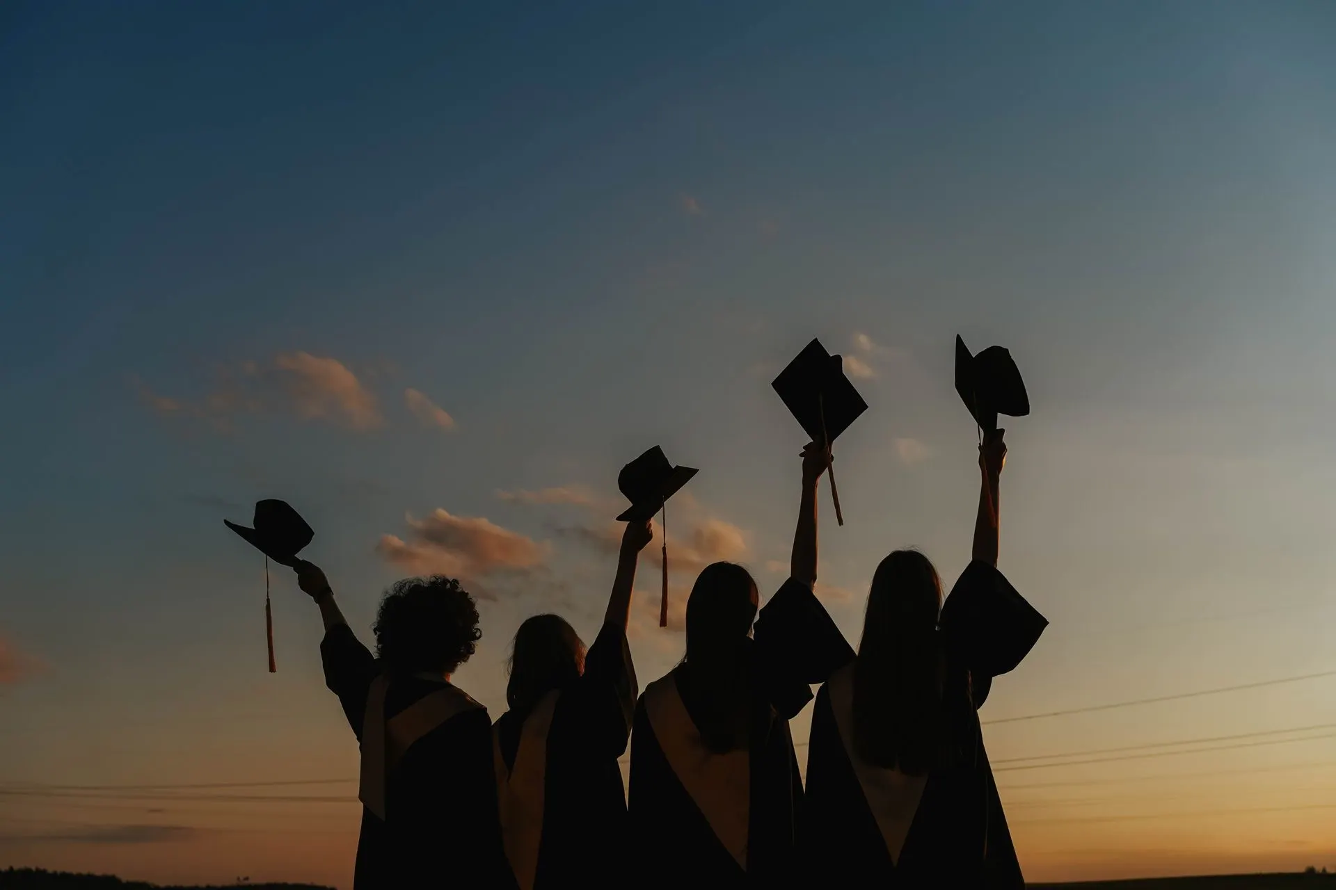 Graduates raise their caps against a sunset sky