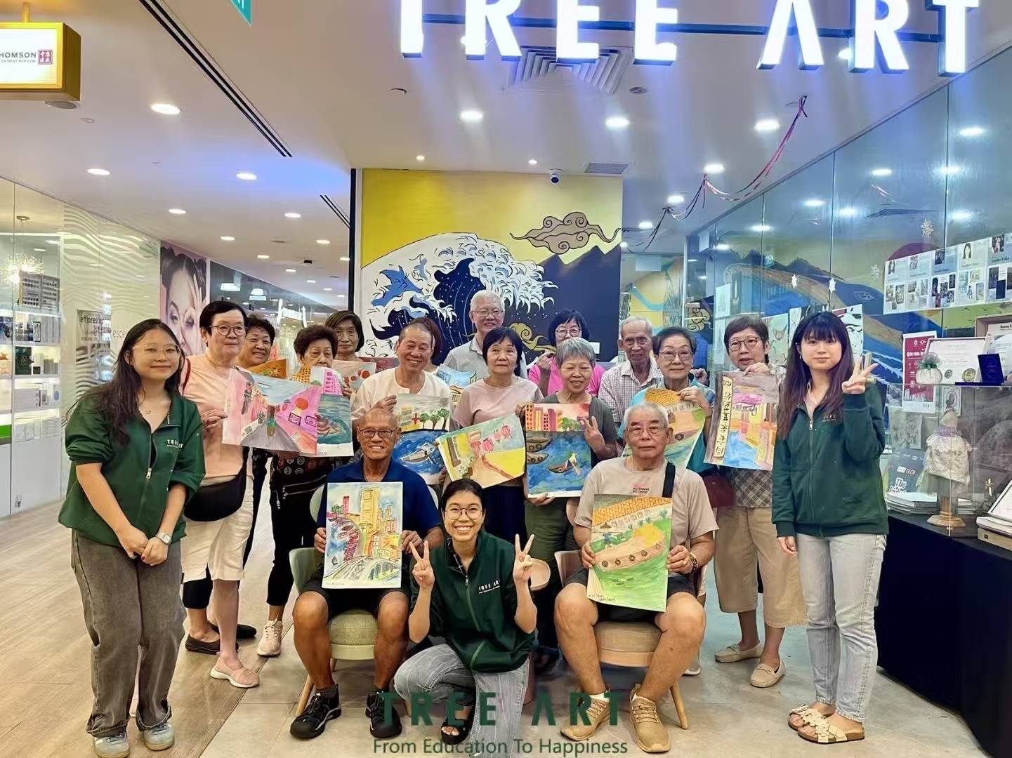 Seniors' Programme students and Tree Art teachers holding their finished watercolour cityscapes outside the TREE ART studio