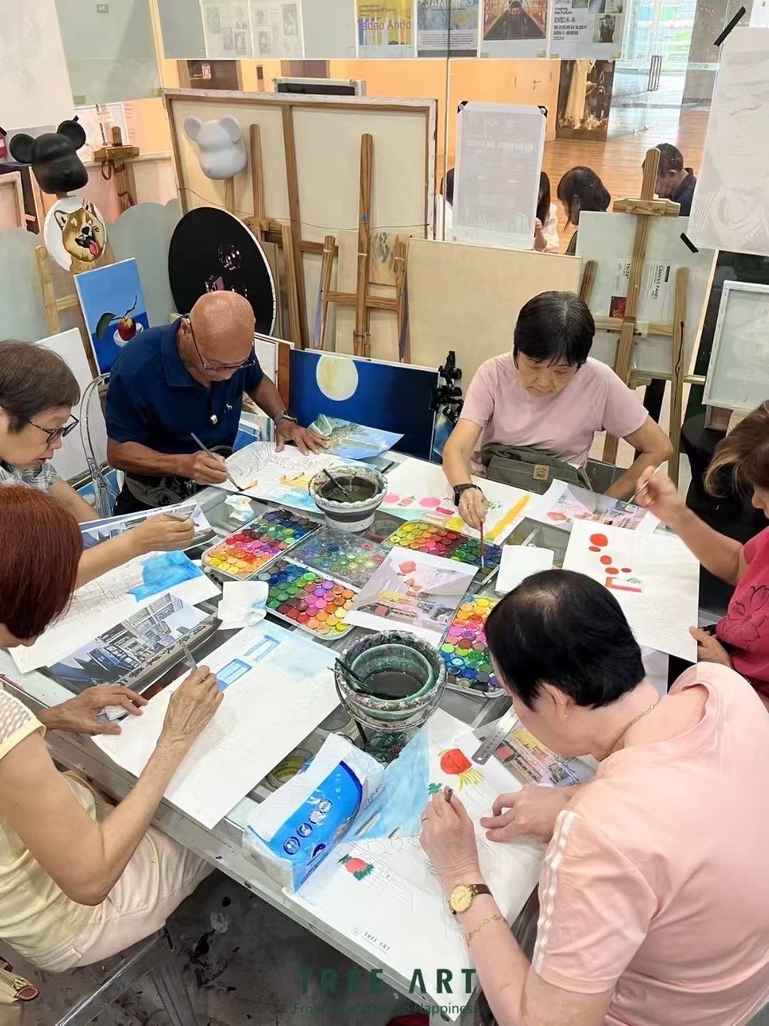 Senior students painting with watercolour palettes around a Tree Art studio worktable