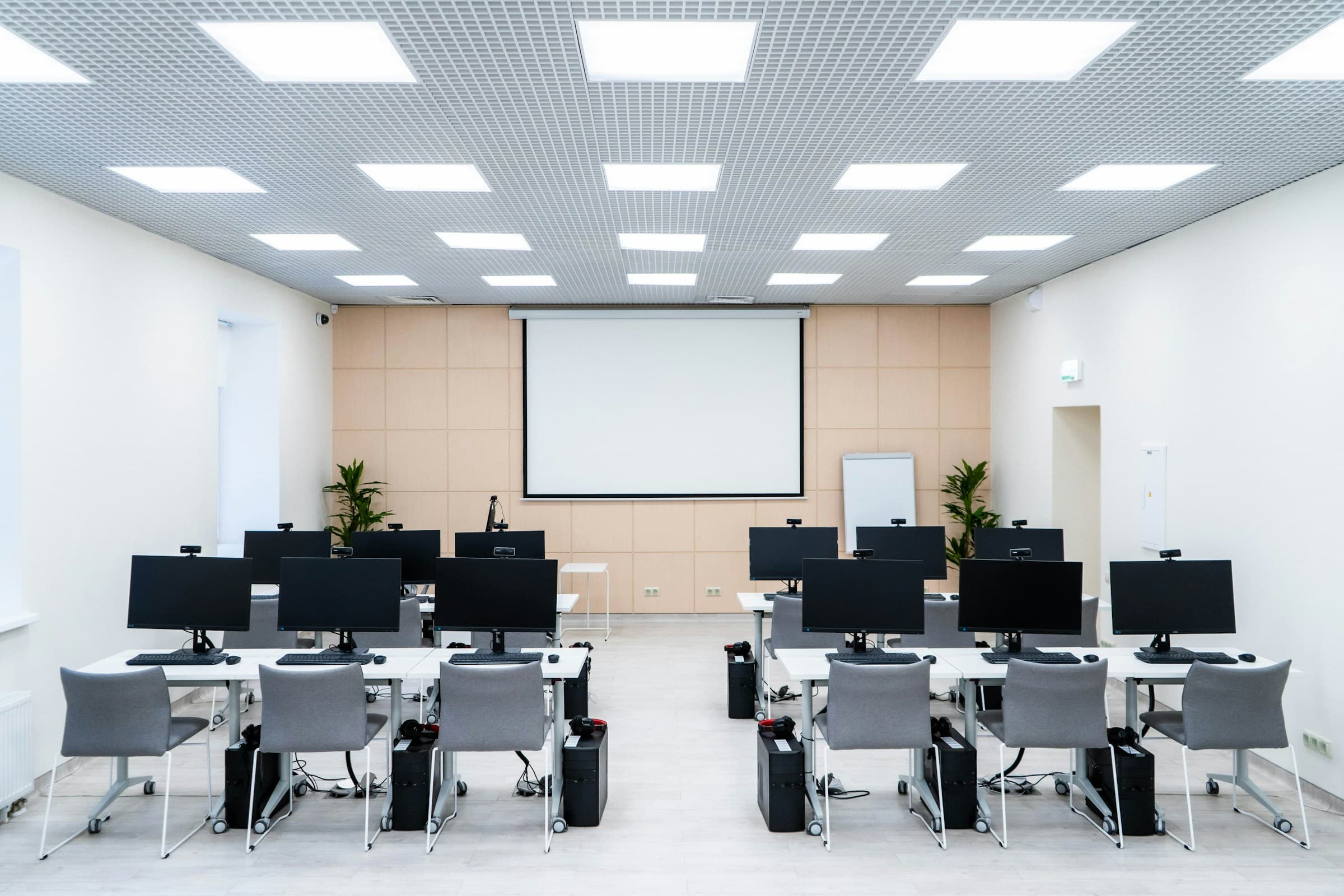 Bright teaching room with rows of screens facing a large projection wall