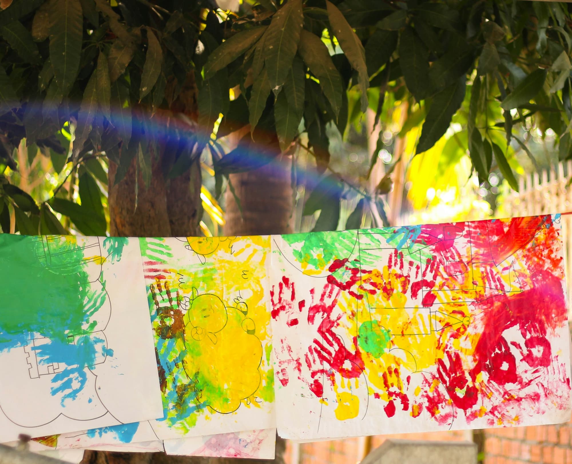 Children's handprint paintings pegged along a line and drying under a tree