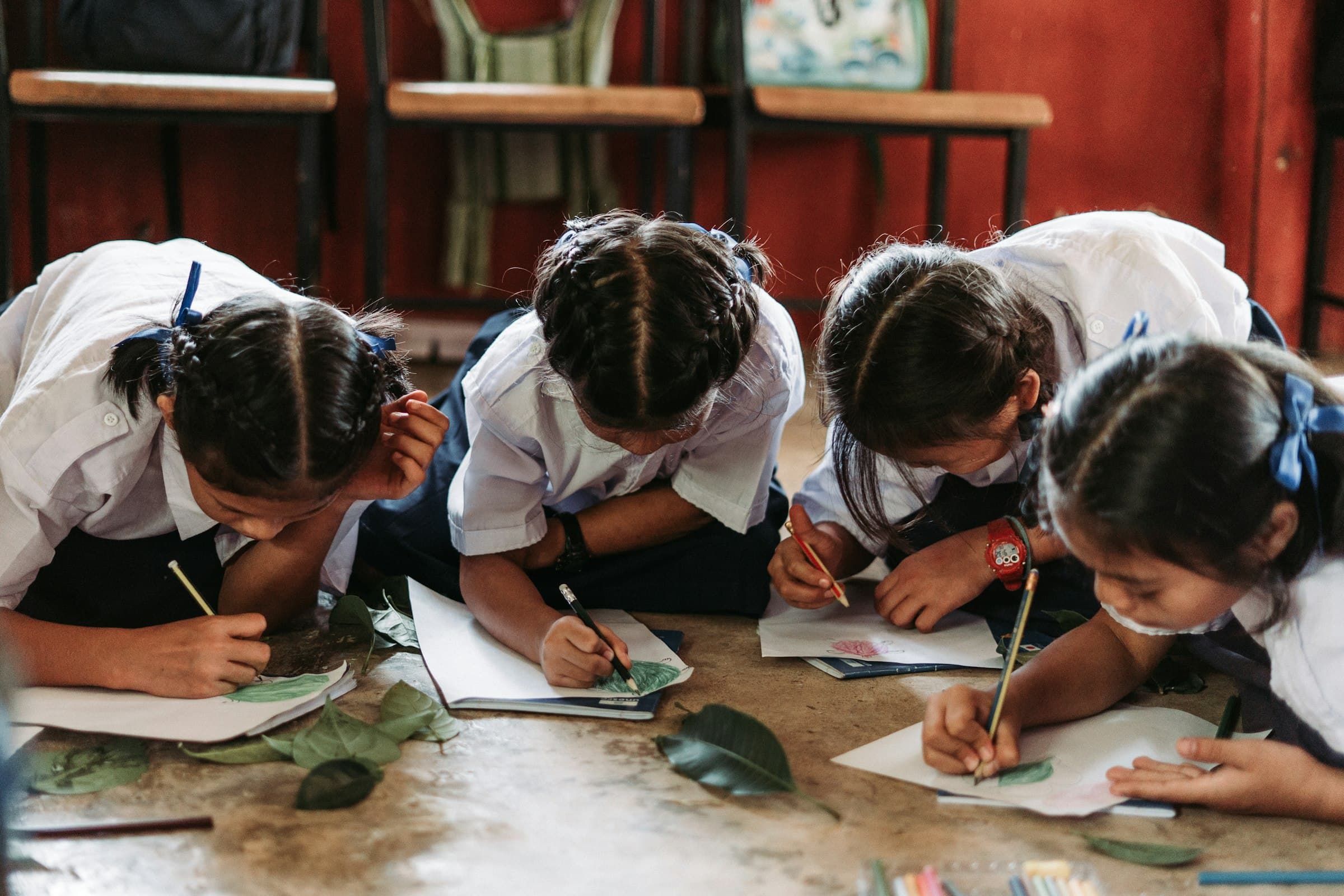 Four children lying on a studio floor, drawing fallen leaves from life in pencil