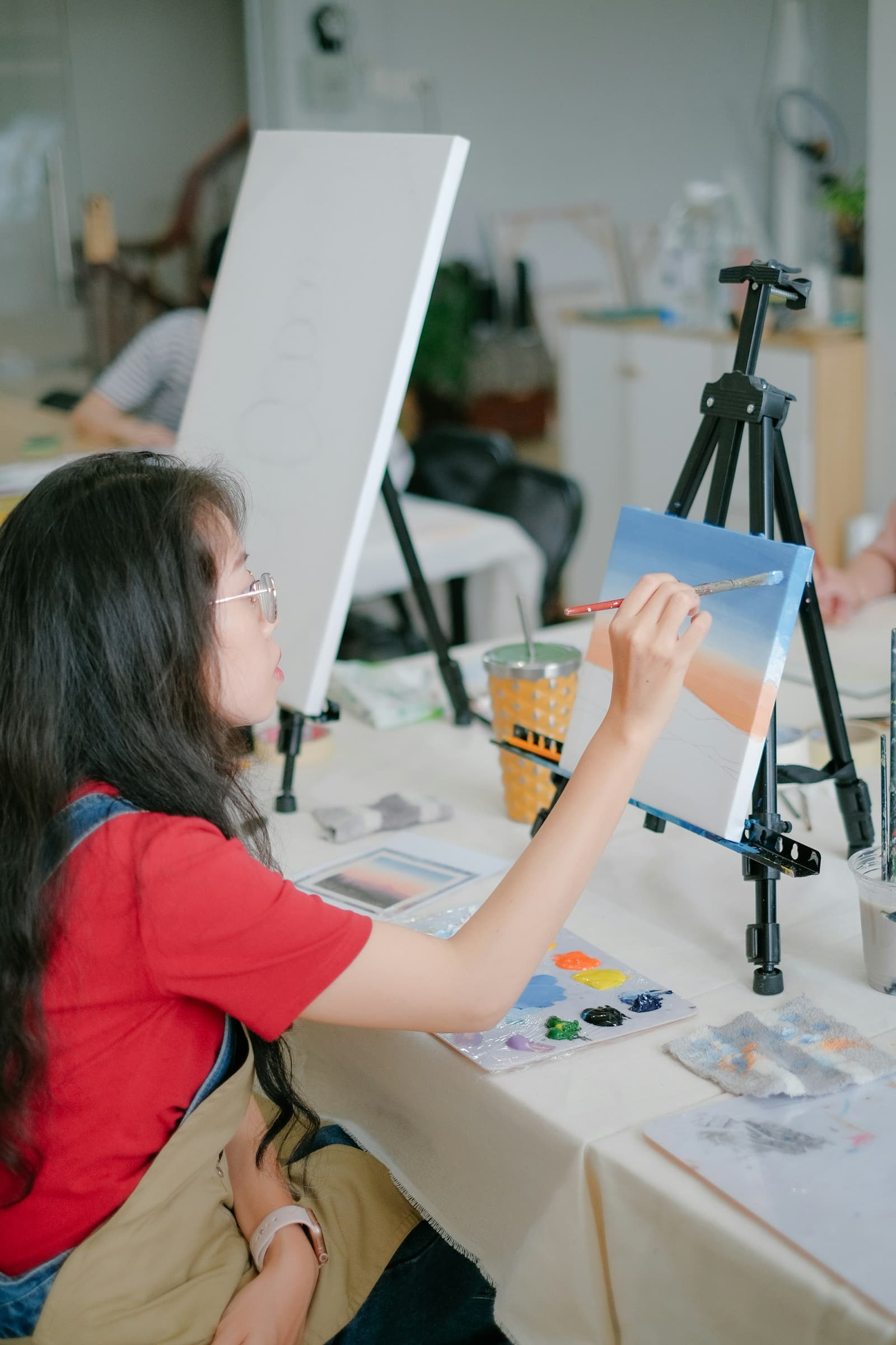 Student painting a landscape on a canvas at a tabletop easel in a daylit studio
