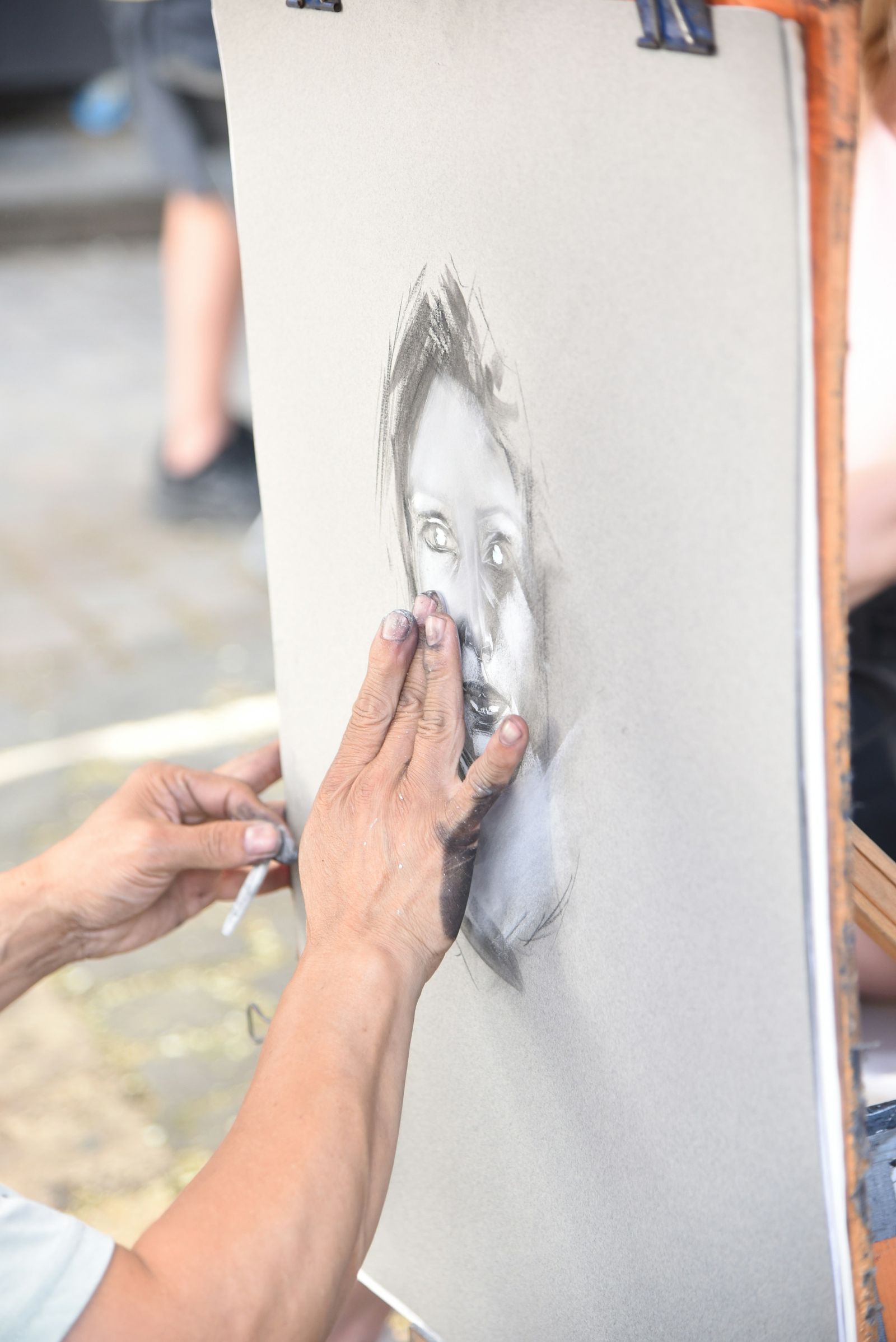 Hands blending a charcoal portrait with fingertips on an easel board
