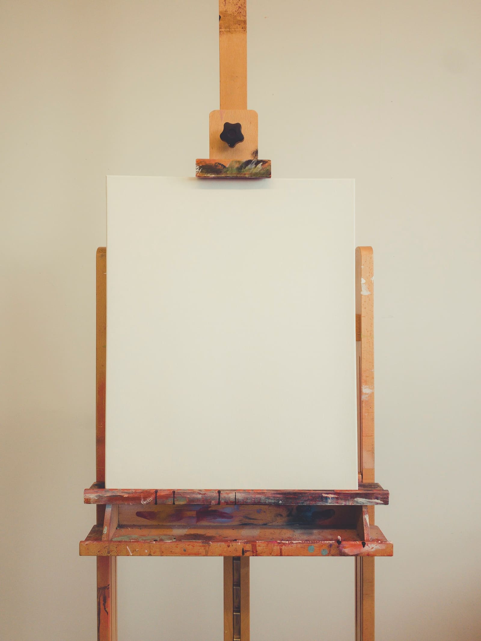 A blank canvas standing on a paint-spattered wooden easel against a cream wall