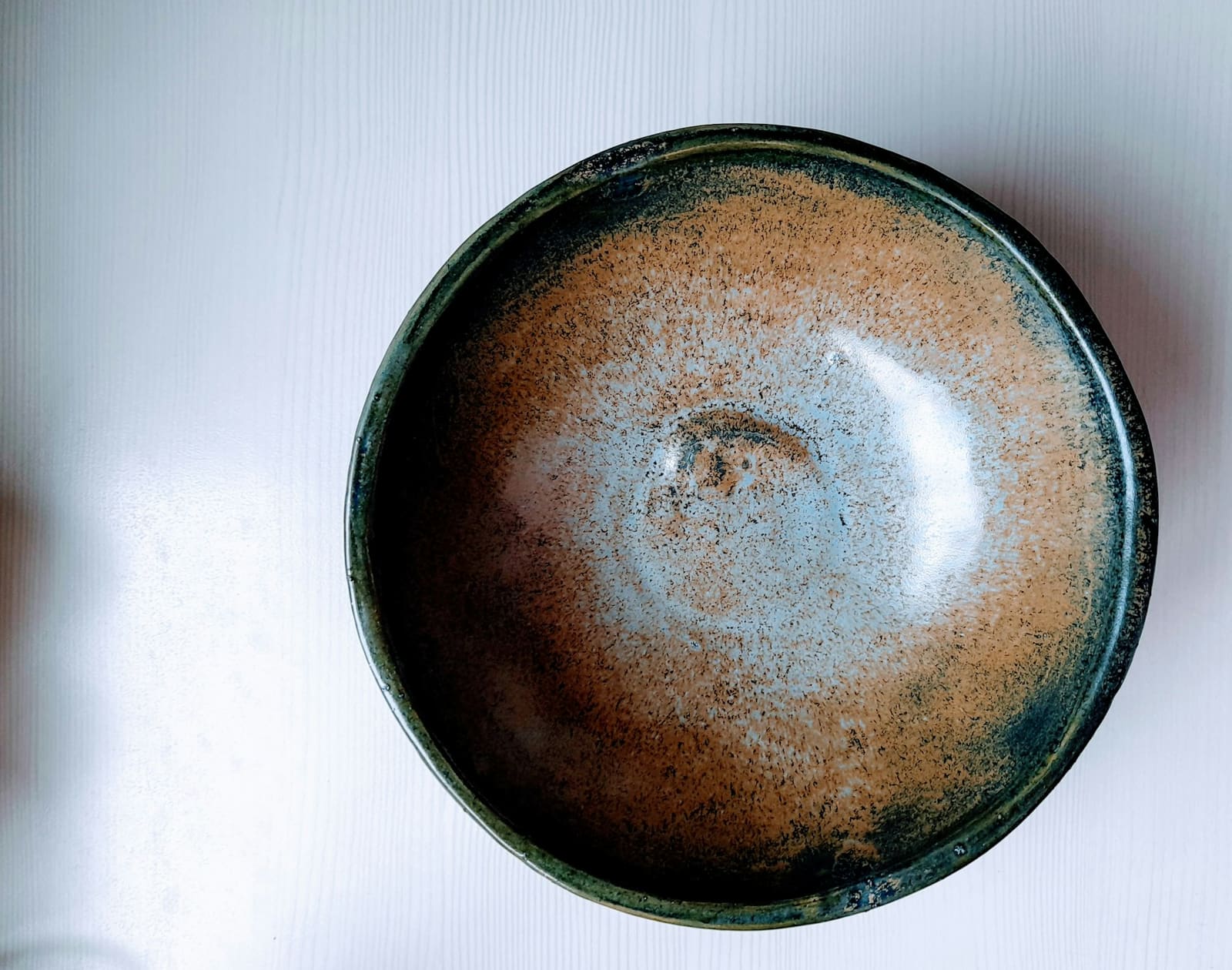 Glazed ceramic bowl viewed from above, its speckled tan centre shading into a deep blue-green rim