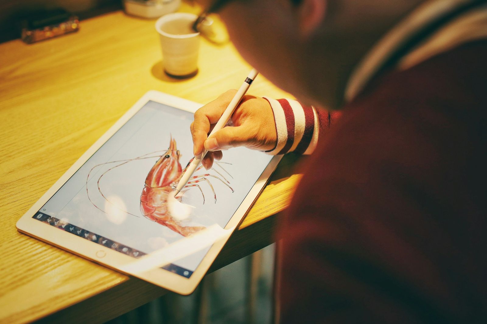 A hand drawing with a stylus on a tablet, a striped prawn illustration on the screen