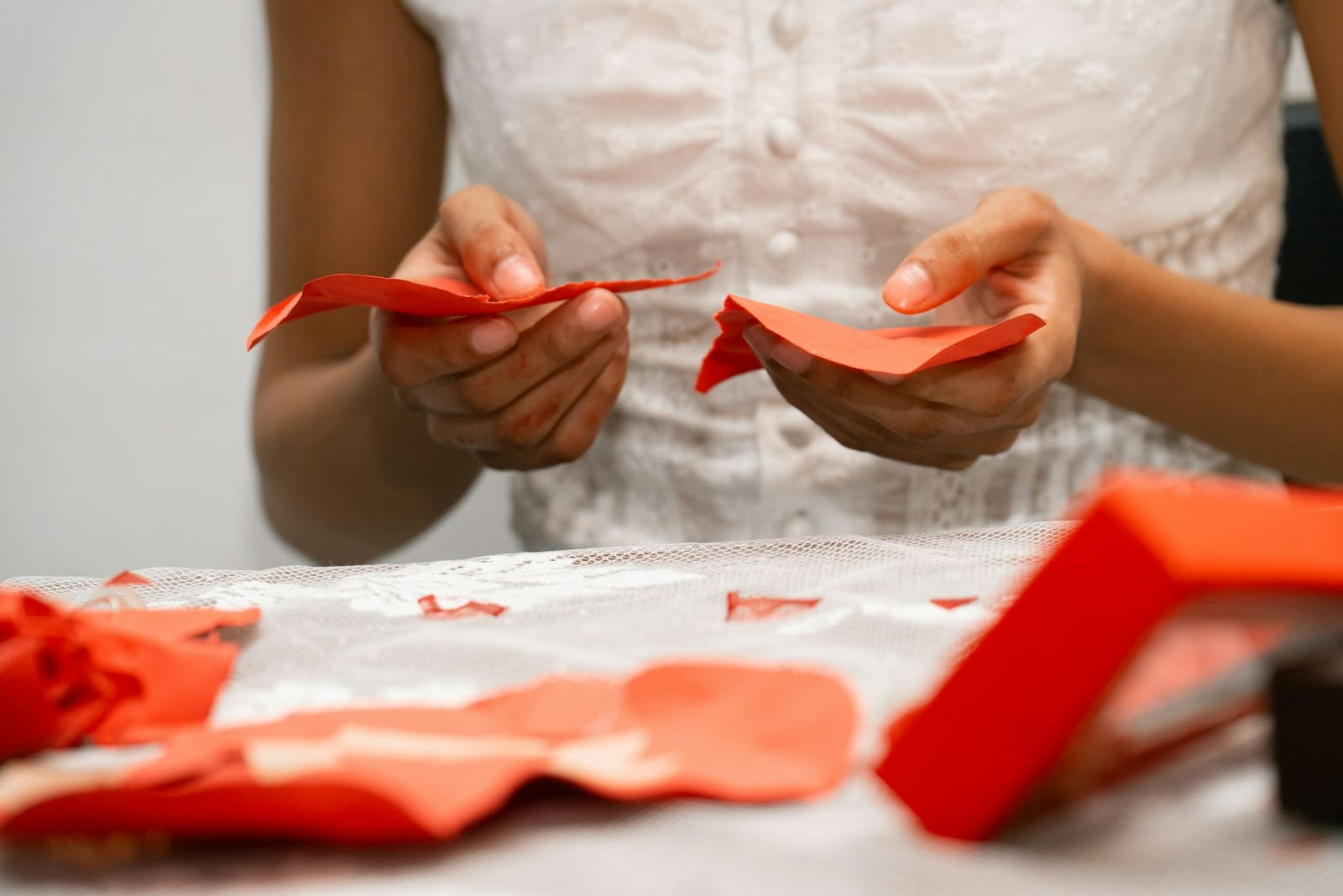 Close-up of a pair of hands curling a piece of red paper above a table strewn with torn paper