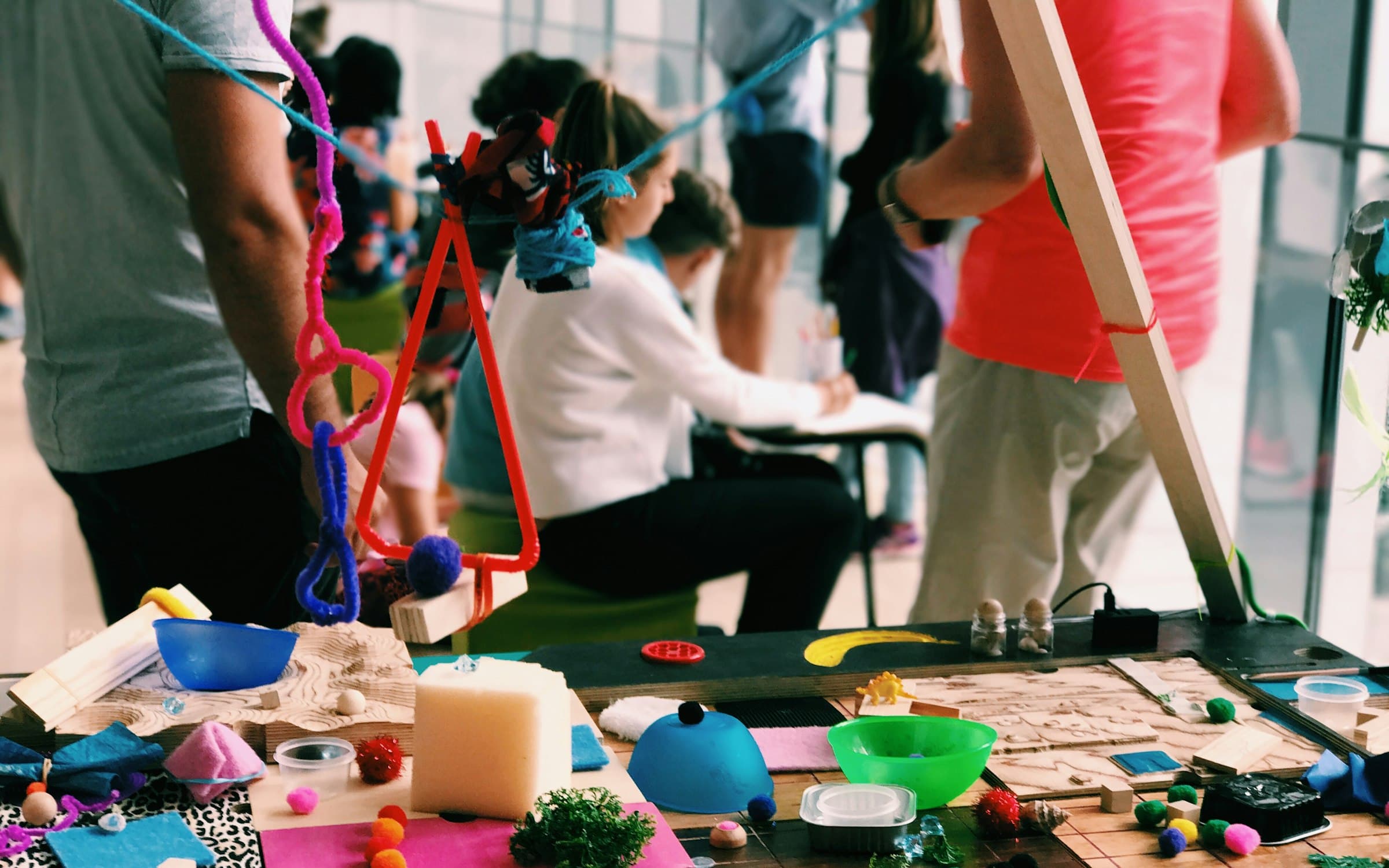 Families crowd around a long activity table strewn with craft materials at a pop-up art workshop