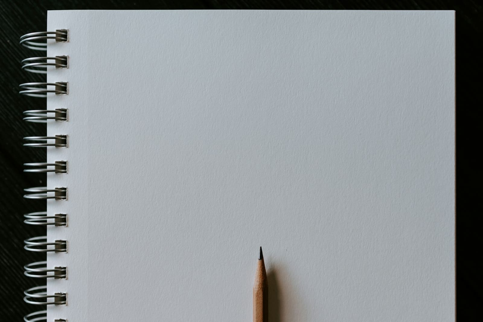 Sharpened pencil resting on a blank page of a spiral-bound sketchbook