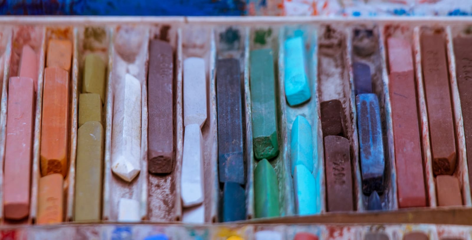 Close-up of a well-used box of soft pastel sticks in oranges, greens, blues and earth colours