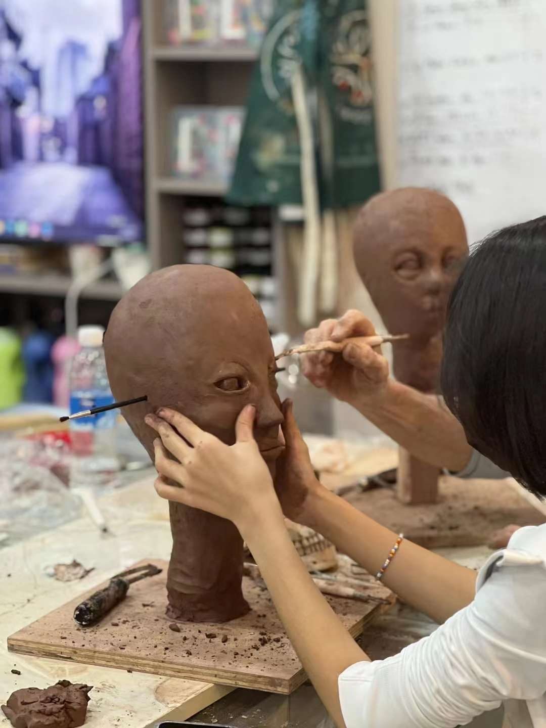 Adult student refining two sculpted clay head studies on a modelling stand