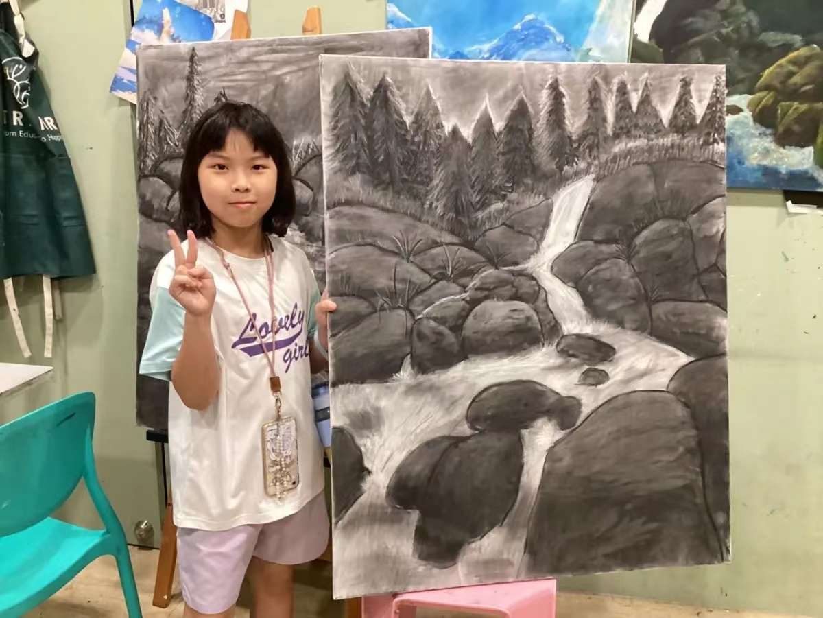 Young student beside two large charcoal landscape studies of pine forests and a rocky stream
