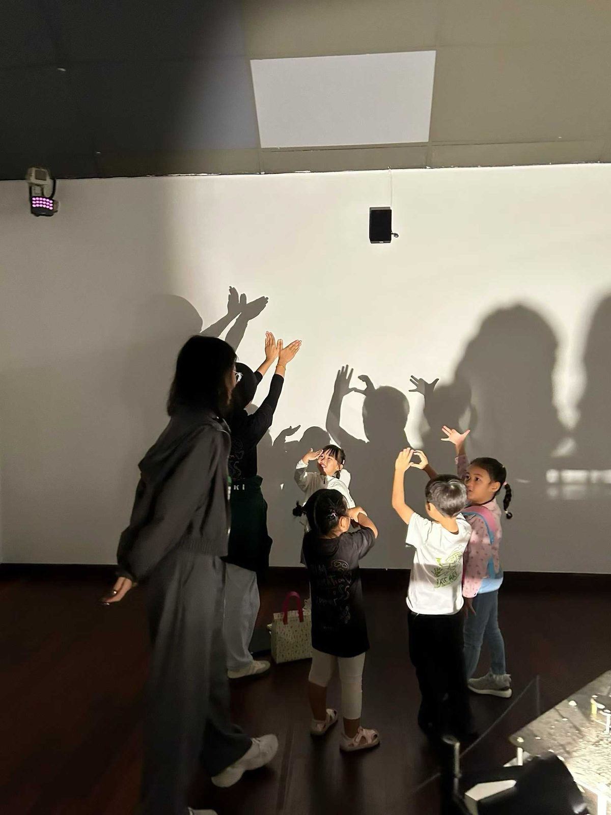 Children casting hand shadows on a glowing wall in a darkened room