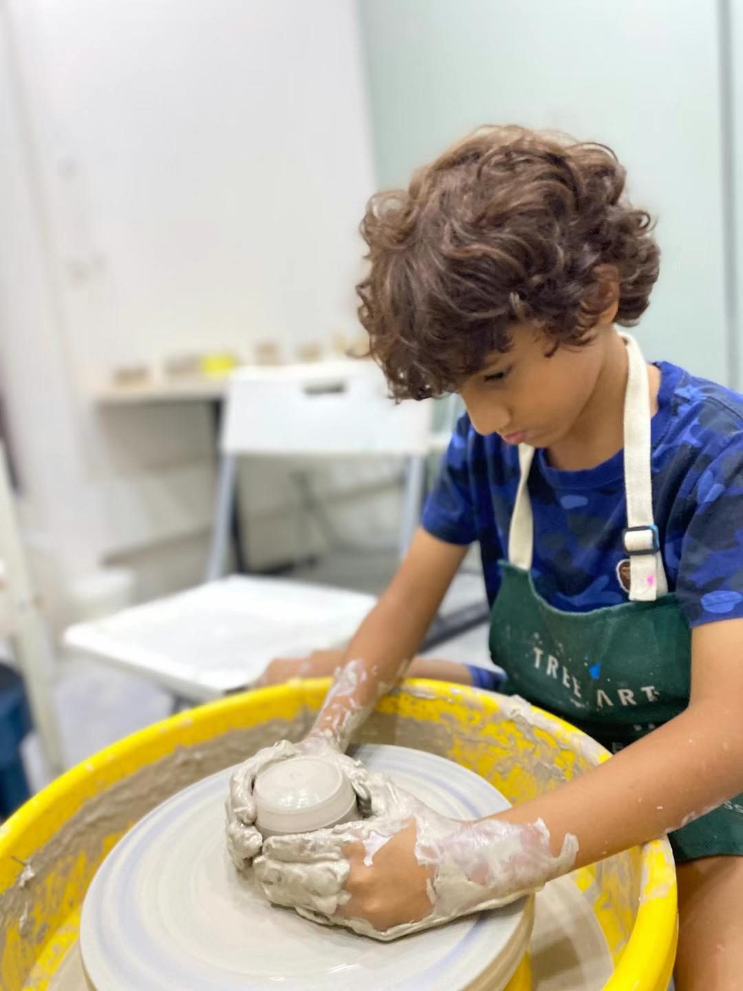 Boy in a TREE ART apron shaping a clay pot on the pottery wheel