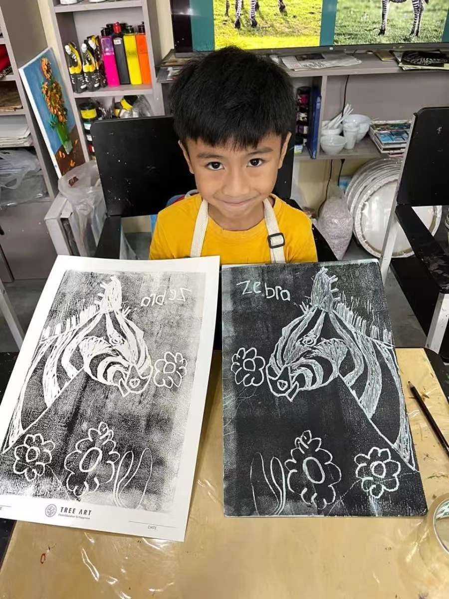 Boy holding up his zebra scratch-art original beside its printed copy in the studio