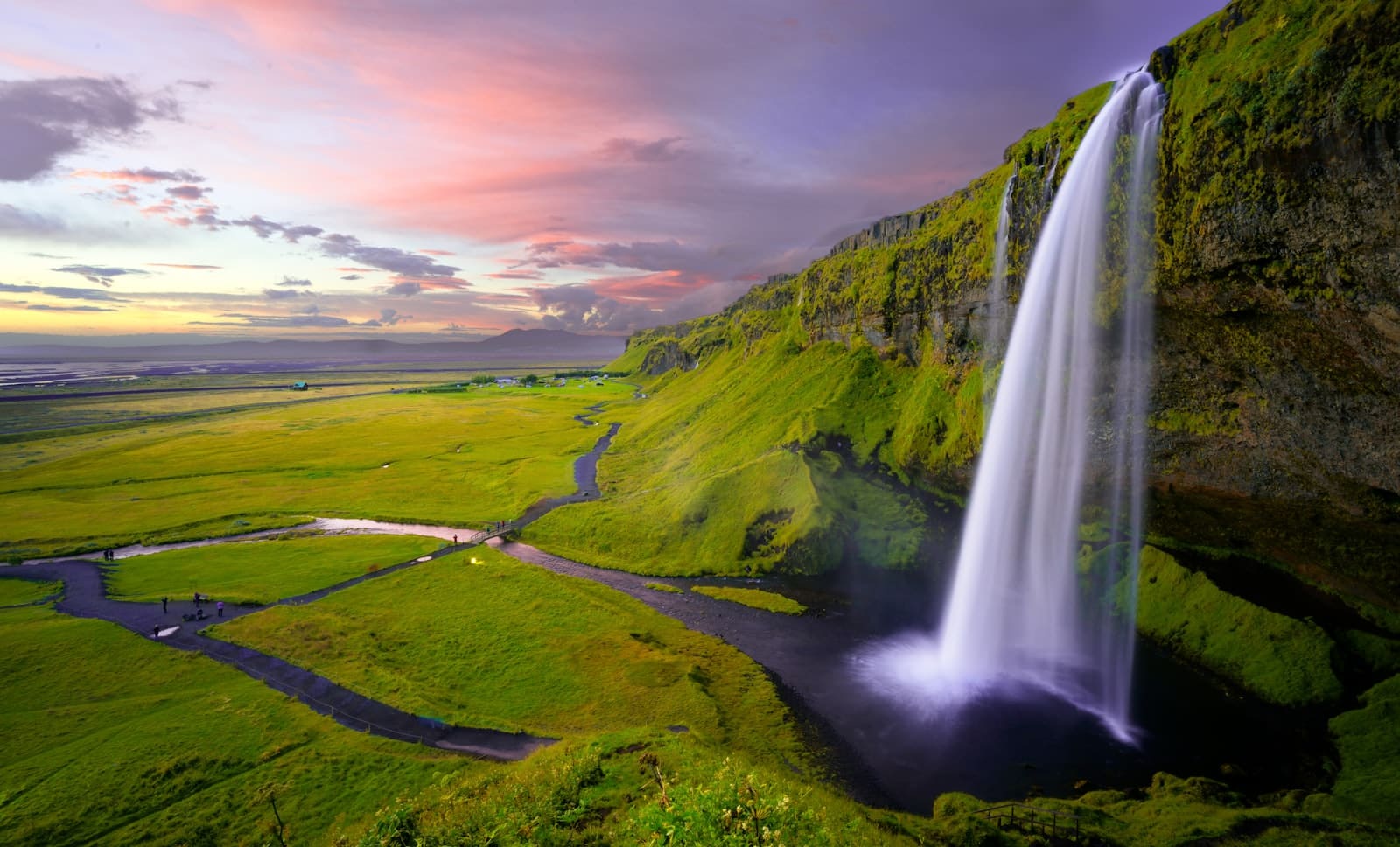 Seljalandsfoss waterfall pouring off a green cliff at sunset