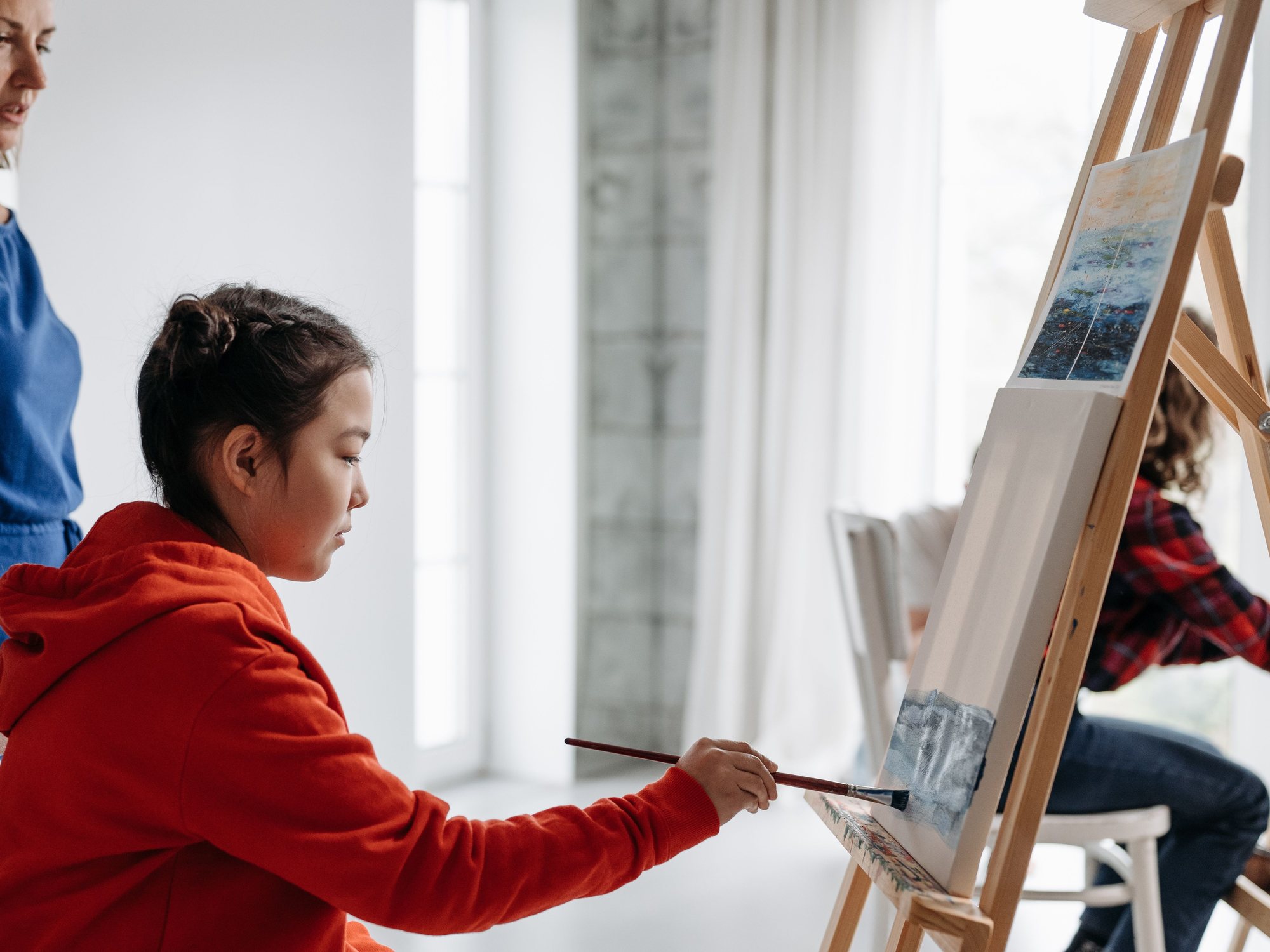 Young girl at an easel, brush in hand, fully absorbed in her painting