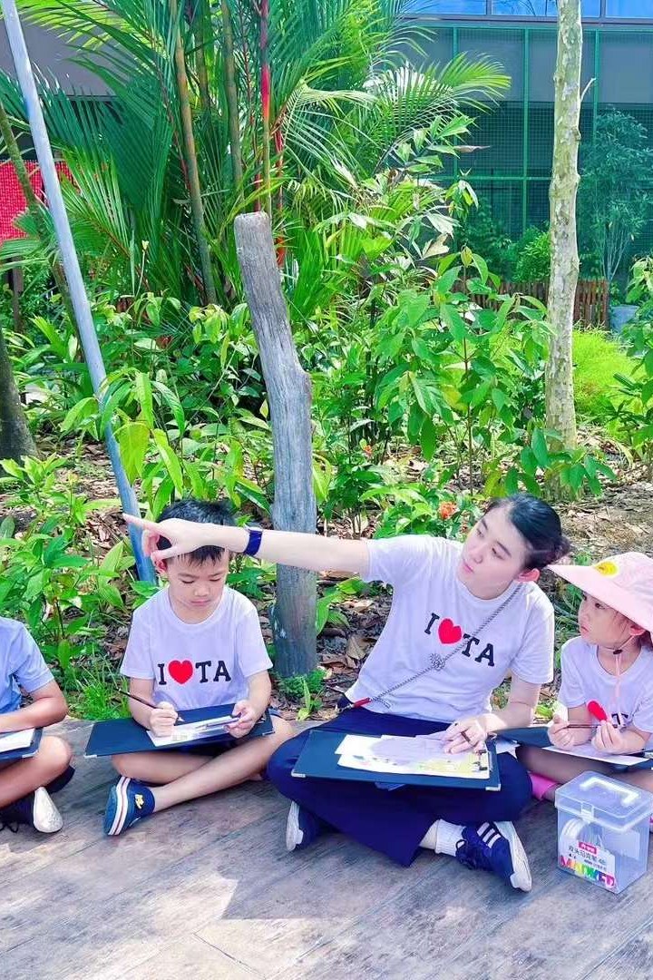 TREE ART teacher pointing out the scenery to children sketching on lap boards along a garden boardwalk